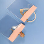 Close-up detail of two open pink EVA ziplock bags showing the rigid pink ziplock closure mechanism, with a pearl and rose gold bracelet visible inside, on a blue surface