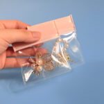 Hand holding an open large pink EVA jewelry ziplock bag containing a crystal leaf brooch and pearl bracelet, demonstrating interior capacity and flexible transparent body