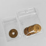 Hand holding a durable clear PVC hanging hole ziplock bag with antique brass coins.