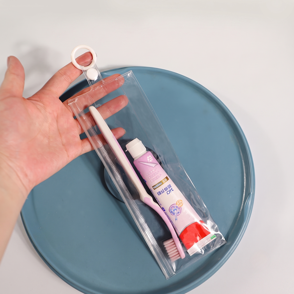 Hand holding a transparent compliant non-phthalate PVC zipper bag travel toothbrush toothpaste kit with hang ring