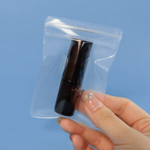 Hand holding a small clear press-to-close cosmetic bag with a makeup tube