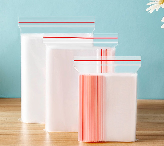 In Stacks of wholesale clear plastic packaging bags with red zipper closures.